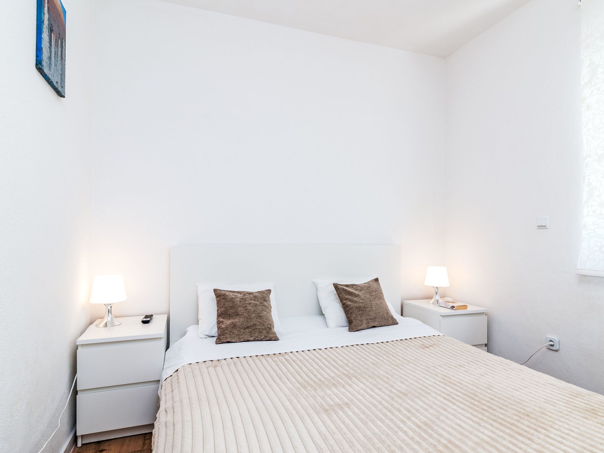 A minimalist bedroom with a bed, two bedside tables, and a nightstand with a lamp.