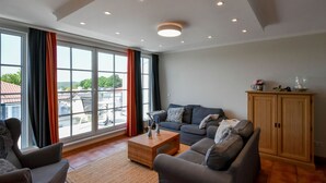 A spacious living room with a large window, a grey sofa, a small coffee table, and a cabinet. - Bernstein by Interhome (Binz)
