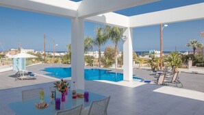 Uma área de piscina no terraço com mesa e cadeiras, vista para o mar e céu claro.