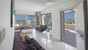 Uma sala de estar moderna com um sofá grande, uma mesa de centro e vista para o mar através de amplas janelas.