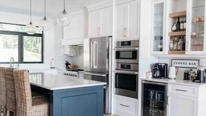 A modern kitchen with white cabinets, a blue island, stainless steel appliances, wicker chairs, and a coffee bar. - Experience Ultimate Luxury at our Exquisite Lakehouse. Large family gatherings! (Erinsville)