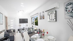 A modern dining area with a glass table set for four, a flat-screen TV mounted on the wall, and a large clock displaying the time. - Moderne 4-Schlafzimmer-Villa im Zentrum von Protaras by Interhome (Protaras)
