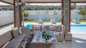 A covered outdoor seating area with a pool, lounge chairs, and a table with drinks and plants. - Moderne 4-Schlafzimmer-Villa im Zentrum von Protaras by Interhome (Protaras)