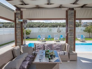 Ein überdachter Außenbereich mit Pool, Liegestühlen und einem Tisch mit Getränken und Pflanzen.