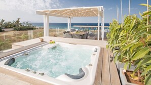 A hot tub with a wooden deck, a pergola with seating, and a view of the ocean.