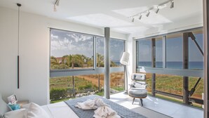 A modern bedroom with a large bed, a view of the ocean, and a balcony with a chair.