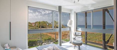 Un dormitorio moderno con una cama grande, vista al océano y un balcón con una silla.