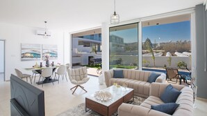 A spacious living room with a large sofa, a coffee table, and a TV. There is a dining area with chairs and a table, and large windows offering a view of the outside. - 3-Schlafzimmer-Villa mit privatem Pool im Zentrum by Interhome (Protaras)