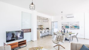 A modern living room with a TV, sofa, and coffee table. There is a dining area with chairs and a table. The room has white walls and a ceiling light. - 3-Schlafzimmer-Villa mit privatem Pool im Zentrum by Interhome (Protaras)