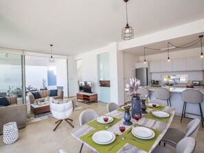 Eine moderne Wohnung mit Essbereich für zwei Personen, einem Wohnzimmer mit Sofa und Couchtisch sowie einer Küche mit Kühlschrank und Mikrowelle.