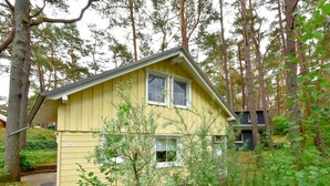 Una casa amarilla de dos pisos con un pequeño porche, rodeada de un bosque denso.