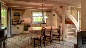Una cocina amplia con vigas de madera, un comedor con mesa y sillas, y una escalera que conduce a un nivel superior.