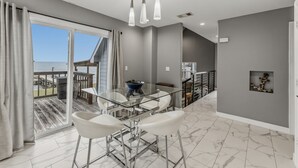 Una cocina moderna con una mesa de comedor de vidrio, taburetes de bar blancos y vistas al mar a través de grandes ventanales.