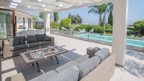 Ein überdachter Außenbereich mit Pool, Sitzgelegenheiten und Meerblick.