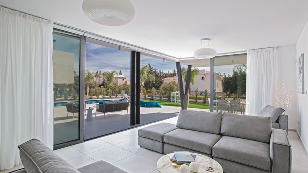 Un soggiorno moderno con un divano grigio, un tavolino da caffè con libri e oggetti decorativi, e vista su una piscina e vegetazione.