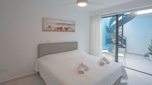 Una camera da letto con un letto, una ventola a soffitto, un quadro e vista su una scala e uno spazio esterno.
