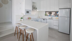 Una cucina moderna con mobili bianchi, un'isola centrale con sgabelli, un forno a microonde integrato e un frigorifero in acciaio inossidabile.