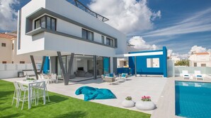 Una moderna casa a due piani con piscina, area salotto esterna e prato curato.
