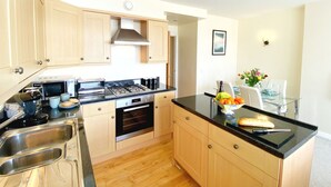 A modern kitchen with wooden cabinets, stainless steel appliances, and a black countertop. - Wohnung mit Meerblick in Torquay by Interhome (Torquay)