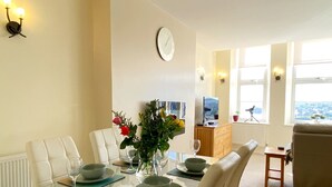 A dining area with a glass table, white chairs, a vase with flowers, and a clock on the wall. - Wohnung mit Meerblick in Torquay by Interhome (Torquay)
