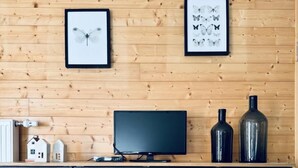 Eine Holzwand mit zwei gerahmten Schmetterlingsbildern, einem schwarzen Fernseher auf einer Holzkommode und zwei schwarzen Vasen darauf.