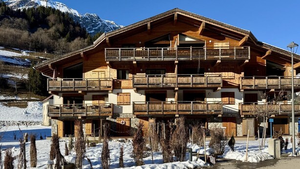 Ein mehrstöckiges Holzchalet mit Balkonen vor einer verschneiten Berglandschaft.