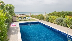 Piscina com vista para o mar, cercada por vegetação e uma rede.