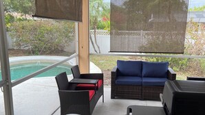 En täckt uteplats med en pool, utemöbler och en grillplats.