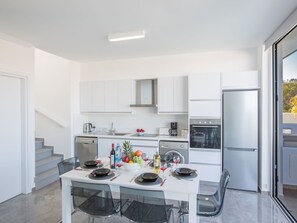 A modern kitchen with white cabinetry, a built-in oven, and a dishwasher. There is a dining table set with plates, glasses, and a bowl of fruit. - Protaras Olivine Villa mit Pool und einem Dachgarten by Interhome (Protaras)