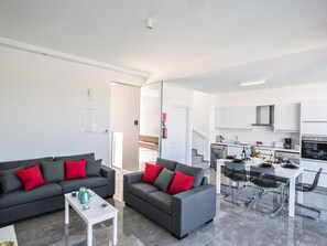 A modern apartment with two grey sofas with red cushions, a white coffee table, a dining area with a glass table and metal chairs, and a kitchen with white cabinets and appliances. - Protaras Olivine Villa mit Pool und einem Dachgarten by Interhome (Protaras)