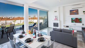 Uma sala de estar moderna com área de jantar, janelas grandes e televisão.