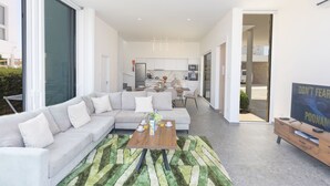 A modern living room with a sofa, coffee table, and a rug. There is a kitchen in the background and a door leading outside. - Luxuriöse Villa Vie Bleu by Interhome (Protaras)
