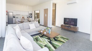 A modern living room with a sofa, coffee table, and television. There is a kitchen in the background with white cabinets and a refrigerator. - Luxuriöse Villa Vie Bleu by Interhome (Protaras)