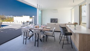 A modern living room with a large TV, a dining area with chairs, and a kitchen area with a bar. - Ferienvilla Vie Bleu mit großem Pool by Interhome (Protaras)