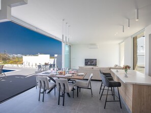 Ein modernes Wohnzimmer mit großem Fernseher, einer Essecke mit Stühlen und einer Küchenzeile mit Bar.