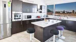 Eine moderne Küche mit dunklen Holzschränken, Edelstahlgeräten, einem großen Fenster und einer zentralen Kochinsel mit Sitzgelegenheiten.