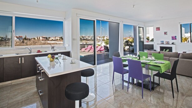 Eine moderne Wohnung mit Küche, Essbereich und Wohnzimmer. Sie bietet große Fenster, einen Balkon und einen Blick auf die Stadt.