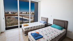 Ein Schlafzimmer mit zwei Betten, einem Balkon mit Blick auf eine Wohngegend und einer Schiebetür.