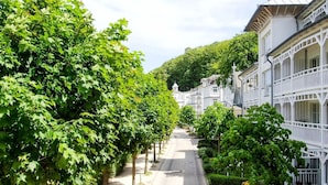 A tree-lined street with white buildings featuring balconies and a central pathway. - Seeschloss Binz Apartment 26, 2 Minuten zum Strand by Interhome (Binz)