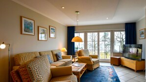 A living room with a sofa, armchairs, a coffee table, a TV, and a large window with curtains. - Seeschloss Binz Apartment 26, 2 Minuten zum Strand by Interhome (Binz)