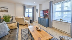 A modern living room with a sofa, a coffee table, a TV, and a large window with curtains. - Die Ellington Court Wohnung by Interhome (Torquay)