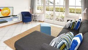 A modern living room with a grey sofa, blue armchair, and a television displaying 'Vollkommend'. - Appartement Sechs in Ostseebad Binz by Interhome (Binz)