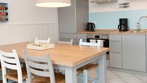 A modern kitchen with a wooden table, white chairs, a coffee maker, and a stove. - Appartement Sechs in Ostseebad Binz by Interhome (Binz)