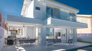 Una casa moderna de dos pisos con un balcón de cristal, una piscina y un patio con mobiliario exterior.