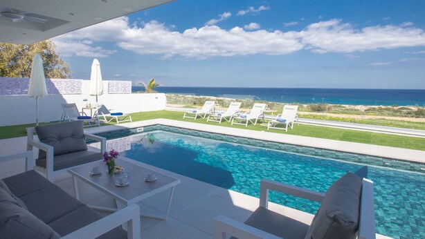 Zona junto a la piscina con vista al océano, mobiliario exterior y ventilador de techo.