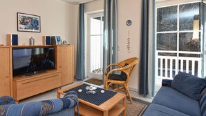 A living room with a television, sofa, and a wicker chair. - Appartement NeunUndZwanzig in Ostseebad Binz by Interhome (Binz)