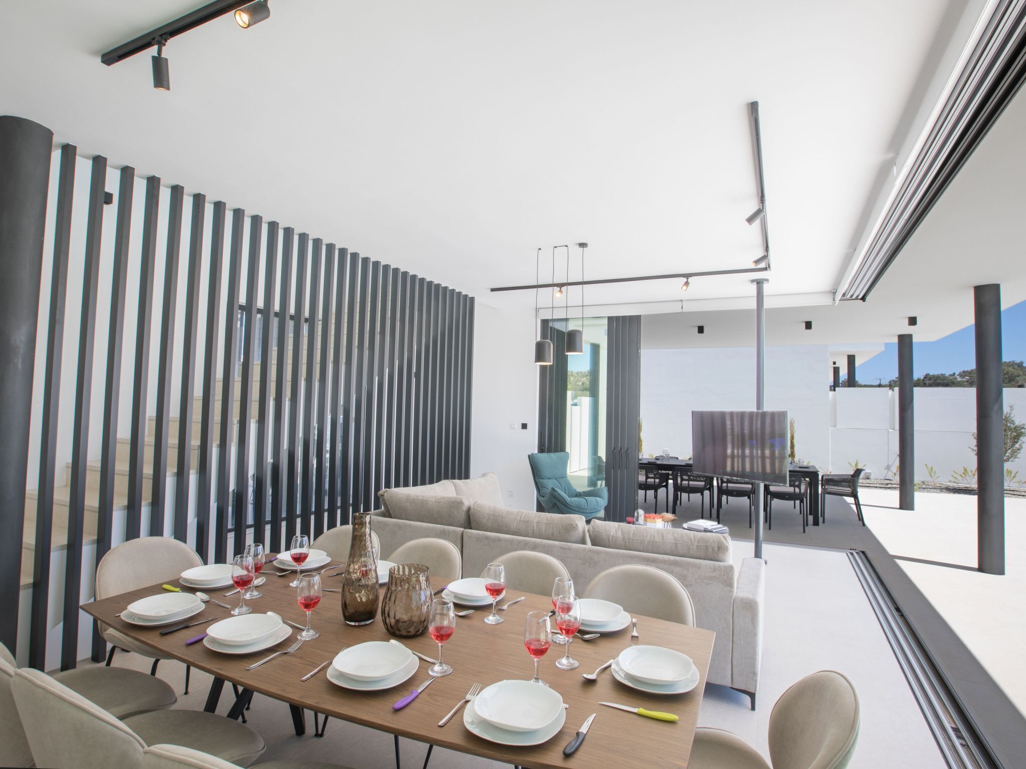 Un espace repas moderne avec une table en bois dressée pour le repas, un canapé et une vue sur l’extérieur.
