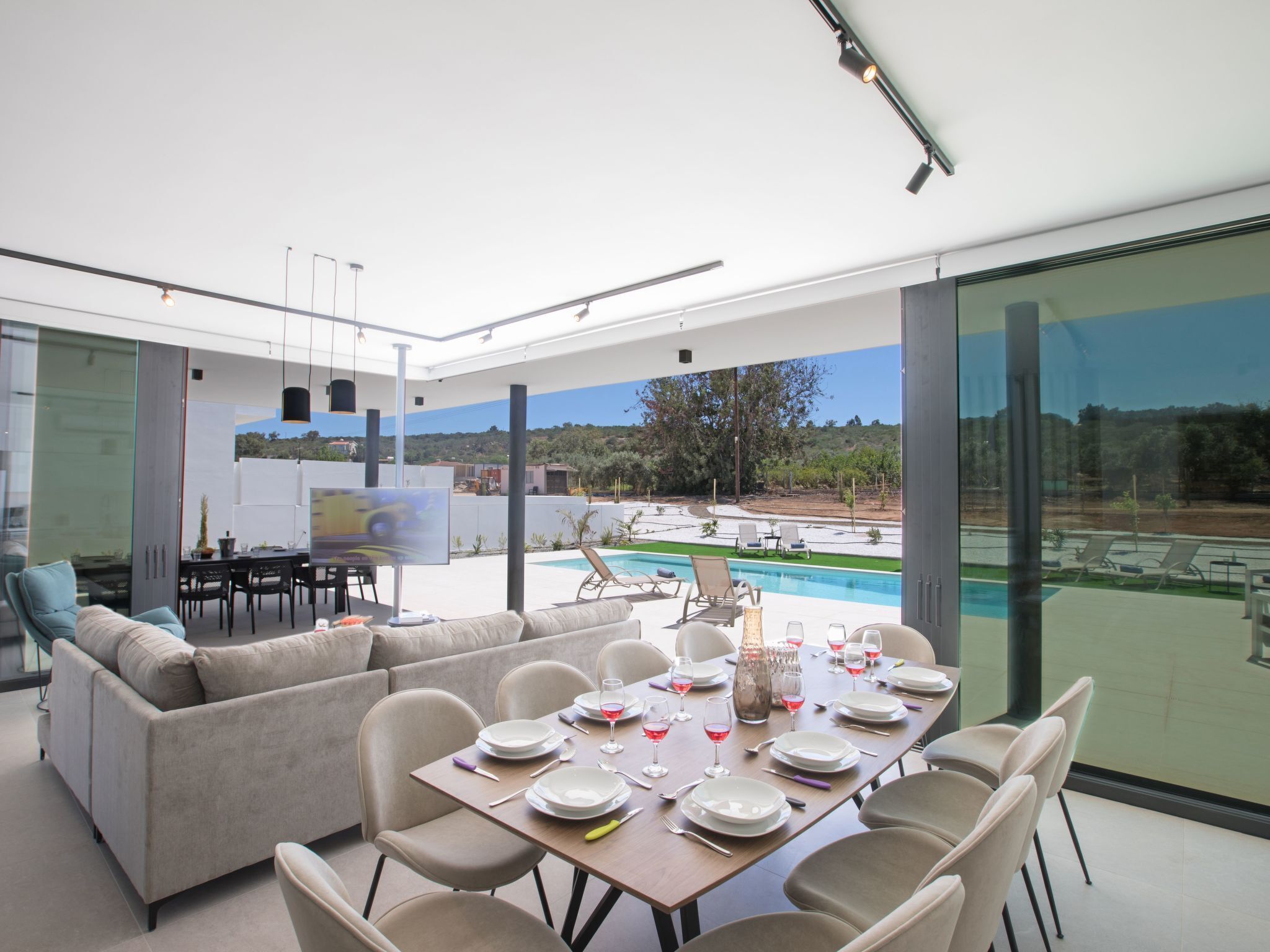 Ein moderner Essbereich mit Blick auf den Pool, eine Couch und ein Tisch, gedeckt für eine Mahlzeit.
