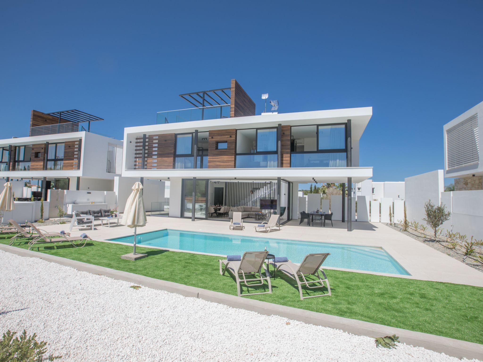 Een modern huis met twee verdiepingen, een zwembad, terras en een verzorgd gazon.