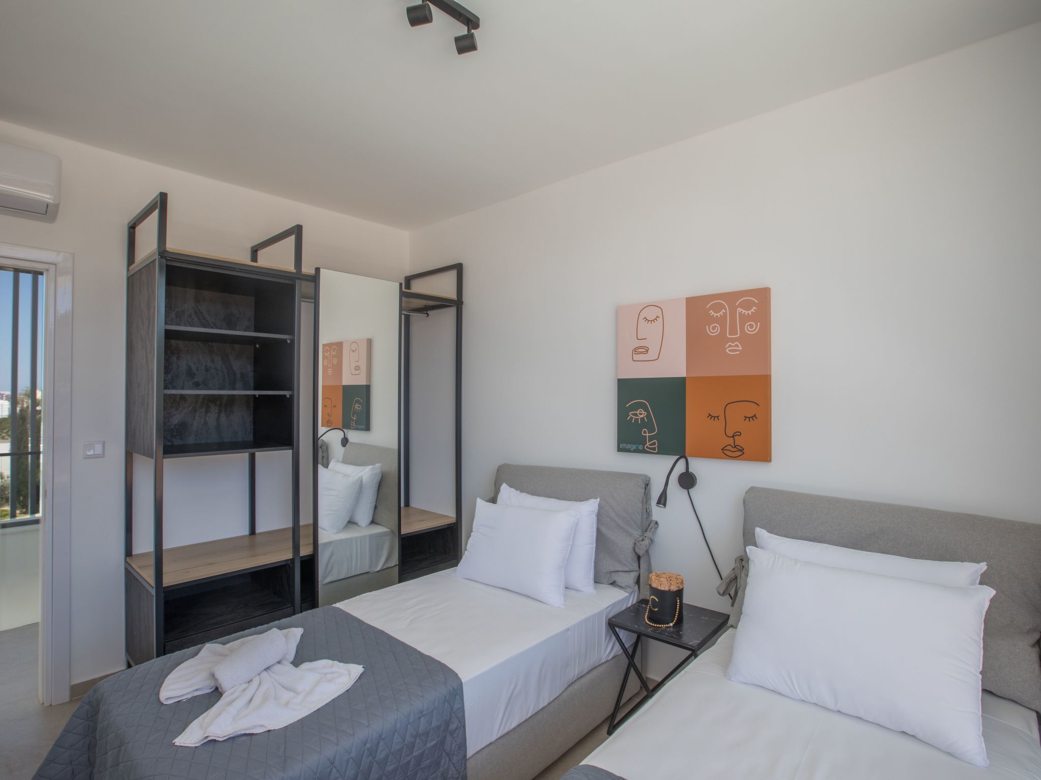 A modern bedroom with two beds, a wardrobe, and a wall art piece.